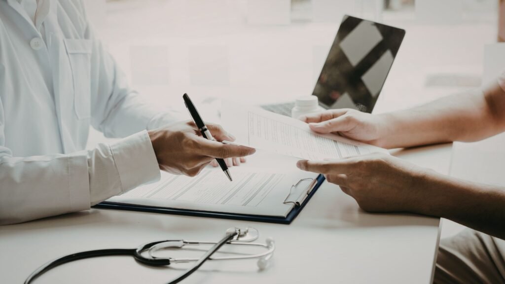 Healthcare provider in white coat writing on medical forms while patient holds X-ray film and paperwork during clinical consultation, stethoscope visible on desk, demonstrating comprehensive patient care including diagnostic assessment and treatment planning