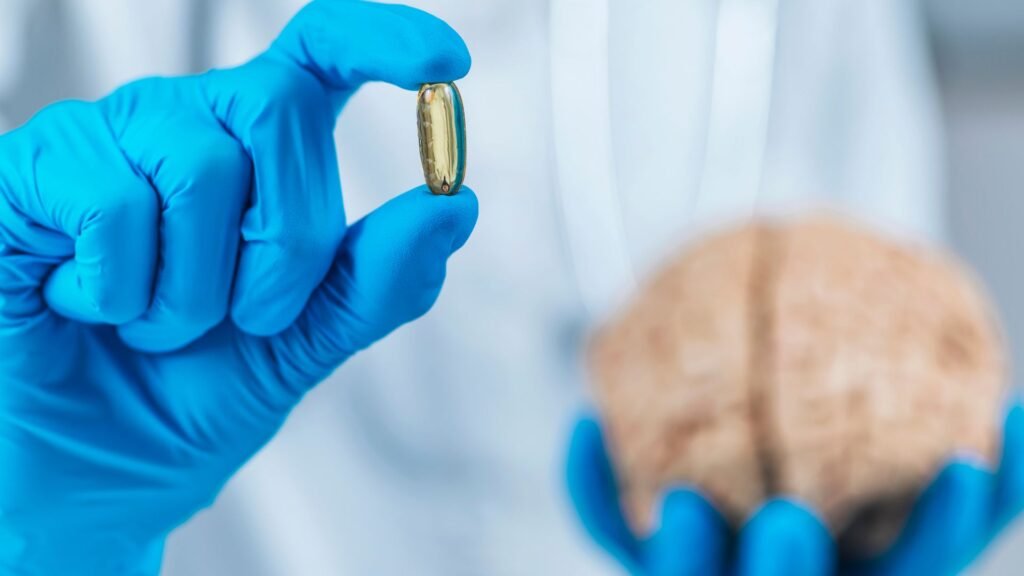 A close-up image of a person holding a golden-colored capsule, potentially omega-3, in one hand, while a brain model is held in the other. This may represent the connection between supplements and cognitive health.