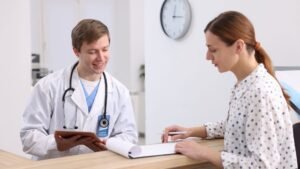 Blog Posts 4 A medical assistant smiles as she assists a patient, handing them paperwork at the reception area of a healthcare facility.