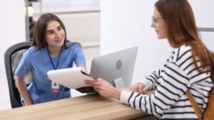 A friendly medical receptionist hands over paperwork to a patient at the front desk of a medical facility.