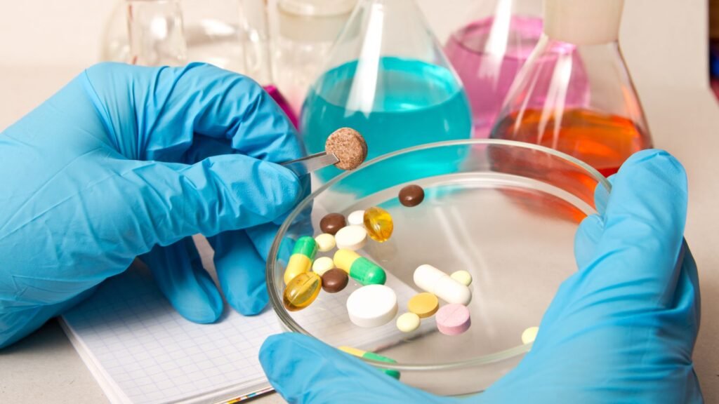 A close-up view of hands wearing blue gloves, carefully handling a pill with a pair of tweezers.